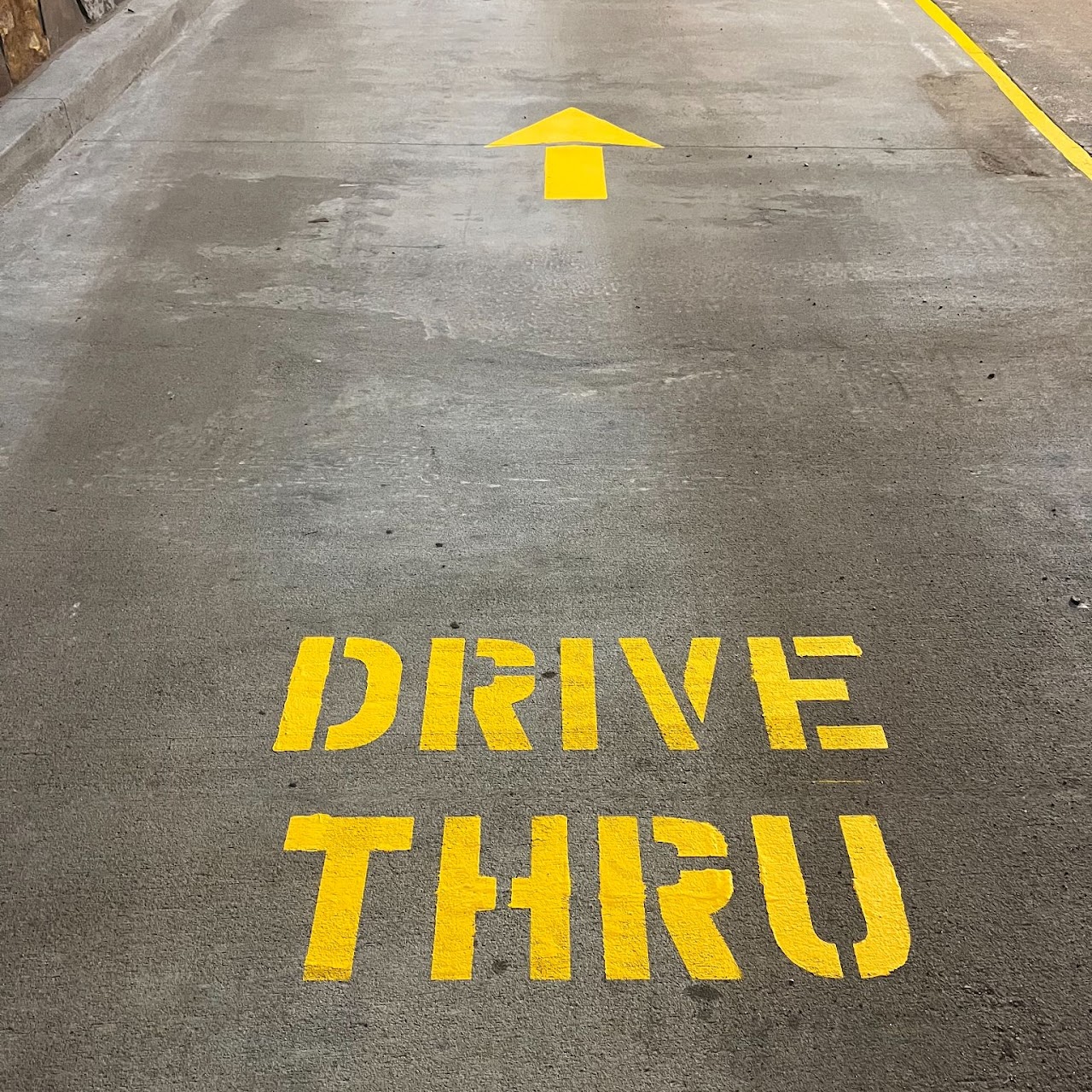 Custom yellow DRIVE THRU stencil with directional arrow painted on concrete